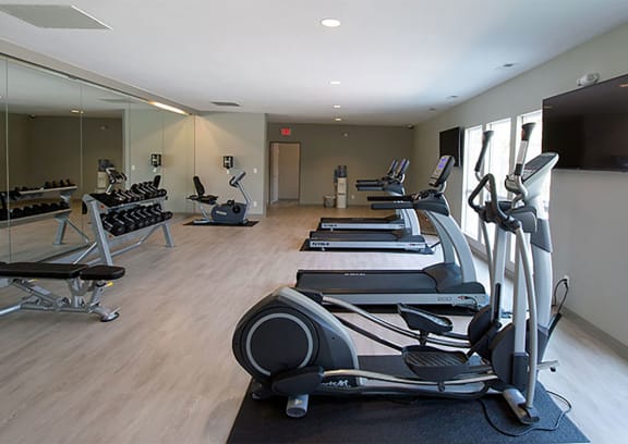 a gym with cardio equipment and a flat screen tv