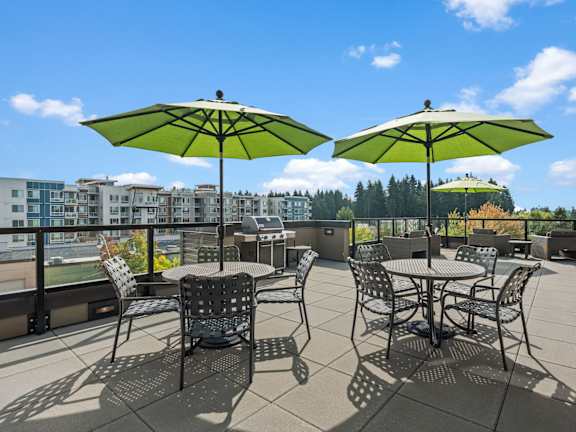 A patio with two tables and chairs under green umbrellas.
