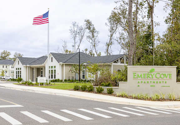 A sign for Emerald Cove Apartments is in front of a building with an American flag.