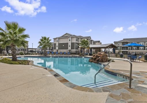 Apartments for Rent New Braunfels TX - Canyon House Apts - Swimming Pool with Rock Feature Surrounded by Concrete, Tile, and Two Small Palm Trees. Features