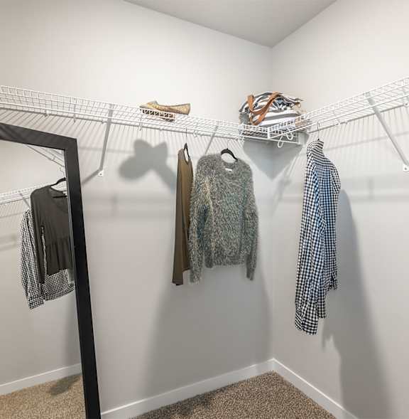A white closet with clothes hanging on a wire rack.