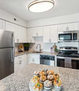 a kitchen with white cabinets and a counter with two stools at Linkhorn Bay Apartments, Virginia Beach, VA, 23451
