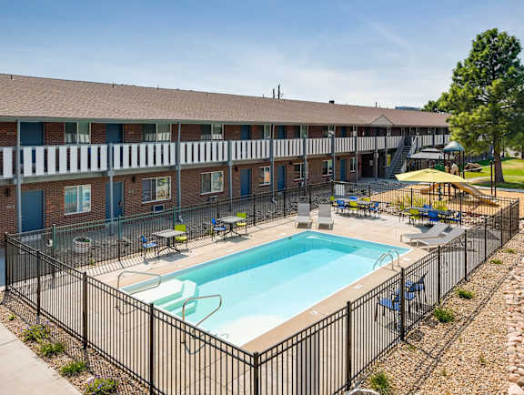 A black fence surrounds a small pool in front of a brick building.
