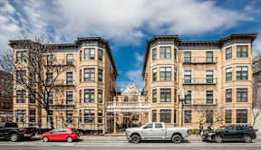 A row of brown buildings with cars parked in front.