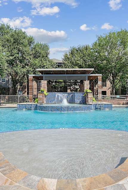 A large swimming pool with a waterfall and a pavilion.