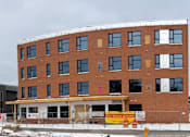 Thumbnail 6 of 16 - A large building with a parking lot in front of it.
