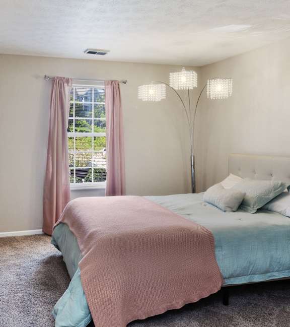 A bedroom with a bed, nightstand, and a desk with a lamp.