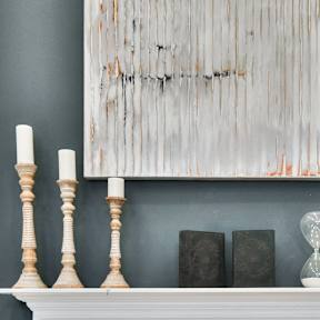 A fireplace with a painting above it and candles on the mantle.