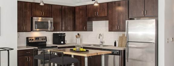 A kitchen with a fridge, stove, and island with a bar stool.
