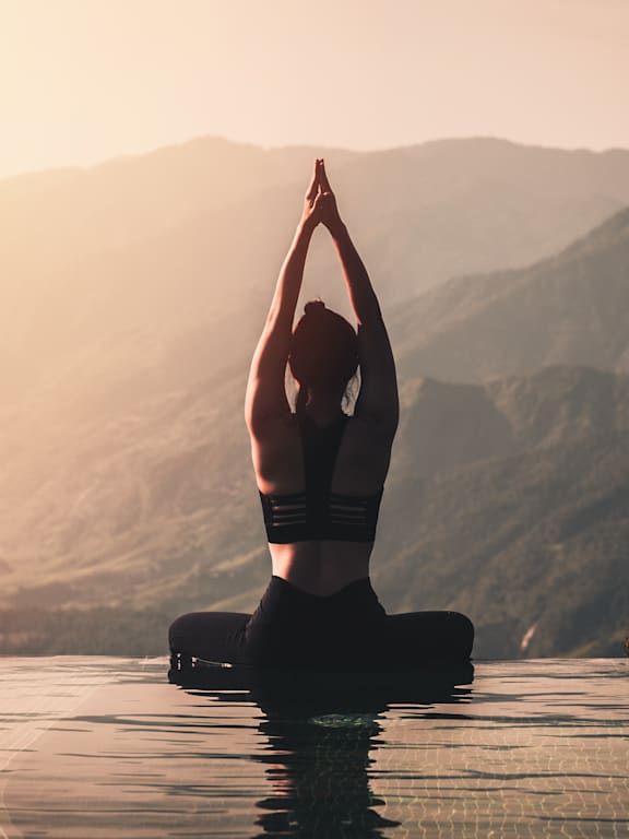 A person is meditating in a pool with mountains in the background.