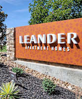 A sign for Leander Apartment Homes is displayed in front of a landscaped area.