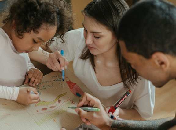 Three people drawing on a piece of paper together.