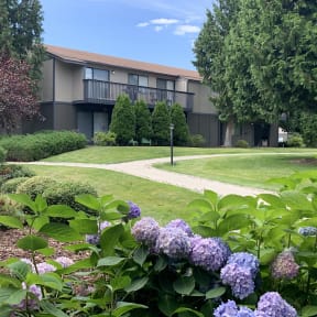 exterior photo of the apartment building with hydrangeas and walking paths