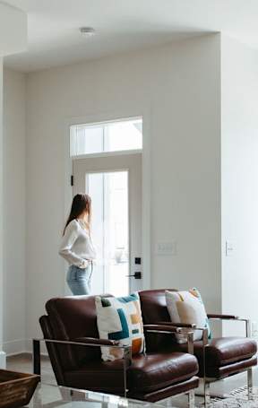 A woman is standing in a living room with a glass coffee table and a brown leather couch.