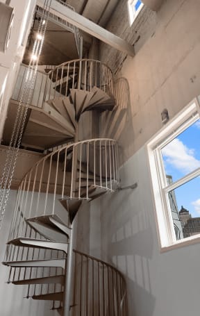 a spiral staircase in a room with two windows and a skyscraper