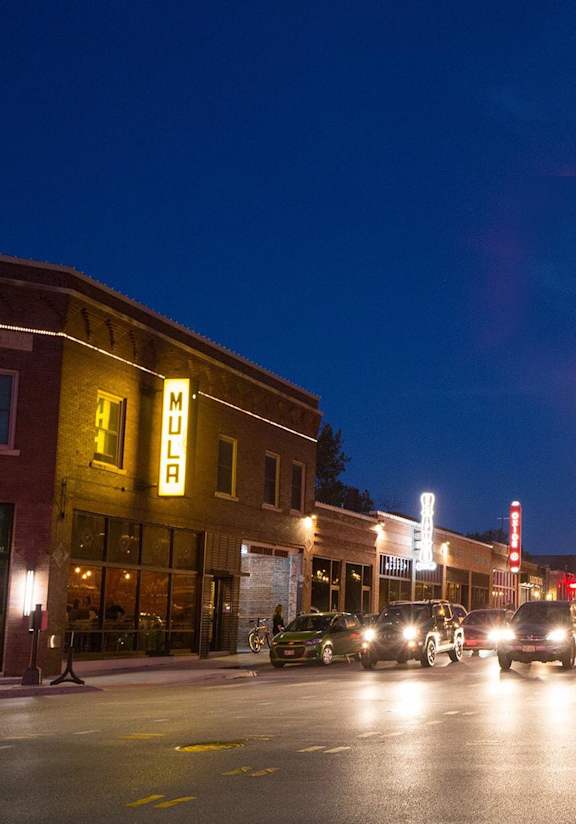 A street scene at night with cars and pedestrians.