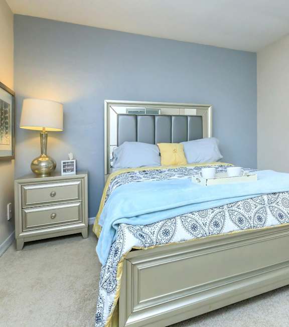 A bedroom with a bed, nightstand, lamp, and wall art.