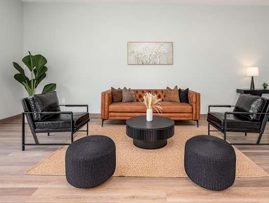 A living room with a brown sofa, black chairs, and a coffee table.