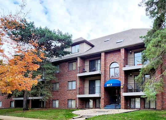 A red brick building with a blue awning and a tree with orange leaves in front.