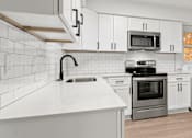Thumbnail 5 of 10 - an empty kitchen with white cabinets and a white counter top