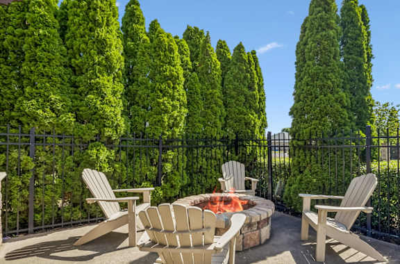 A patio with a fire pit surrounded by trees.