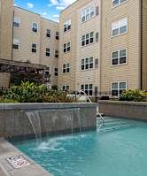 A pool with a waterfall in the middle of a courtyard surrounded by buildings.