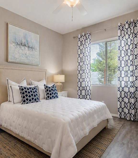 A bedroom with a bed, nightstand, and a plant. at Vistoria At Stadium Apartments, Glendale, Arizona