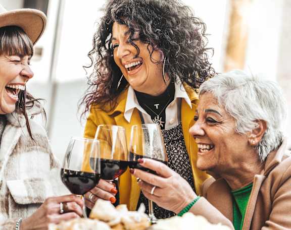 Three people are laughing and toasting with wine glasses.