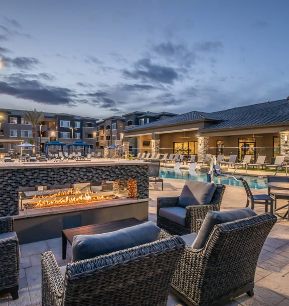 a patio with chairs and a fire pit at night