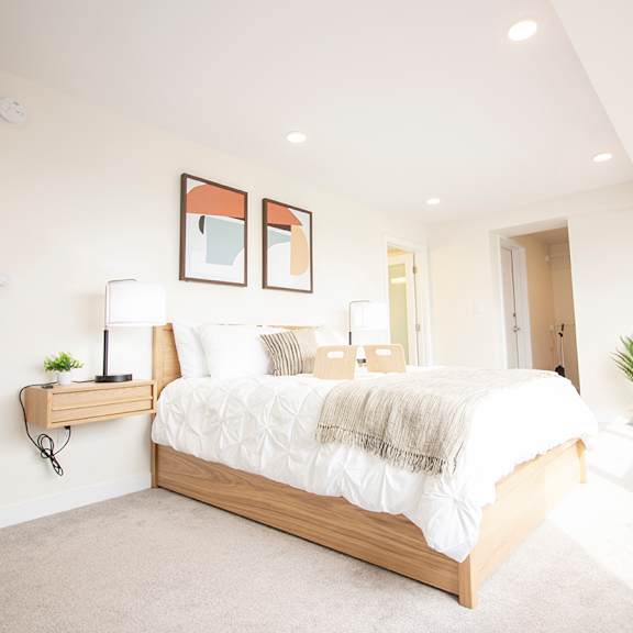 A bedroom with a large bed, a painting on the wall, and a wooden floor.