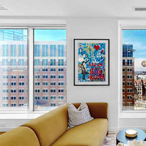 A living room with a yellow couch and a painting on the wall.