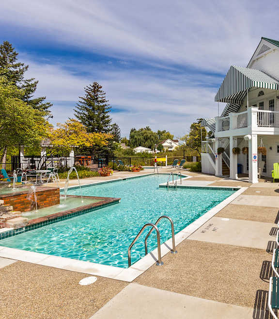 A large white building with a green roof is behind a pool.