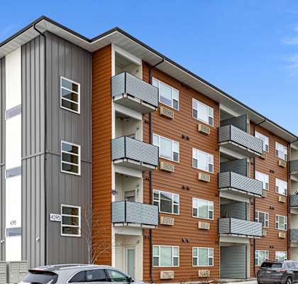A silver car is parked on a street in front of a multi-story apartment building.
