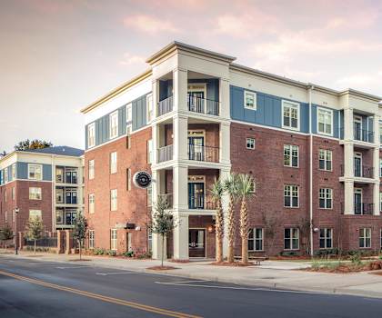 an exterior view of a brick apartment building with green grass and trees at The Standard, South Carolina