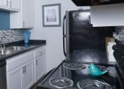 Thumbnail 7 of 23 - Fifteen 50, 89119 - Kitchen in Las Vegas apartment near strip with black and silver appliances, tile backsplash, and colorful modern vases on counters