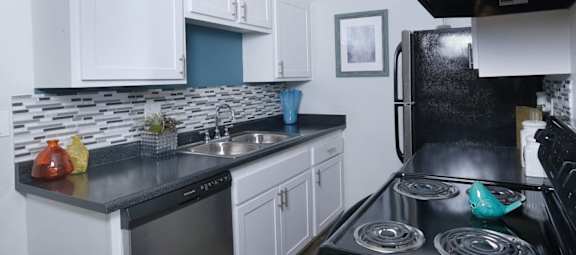 Fifteen 50, 89119 - Kitchen in Las Vegas apartment near strip with black and silver appliances, tile backsplash, and colorful modern vases on counters