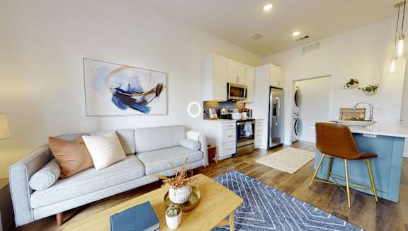 A living room with a white couch, a blue chair, and a painting on the wall.