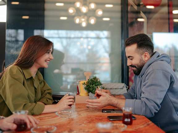 A man and a woman are sitting at a table in a restaurant, enjoying a meal and drinks together.