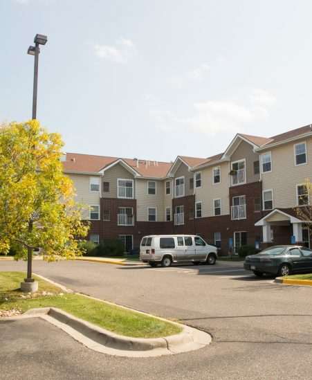 A parking lot in front of apartment buildings with a tree in the foreground.