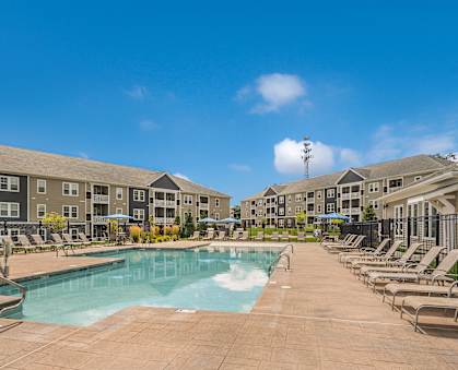 A large swimming pool surrounded by sun loungers and apartment buildings.