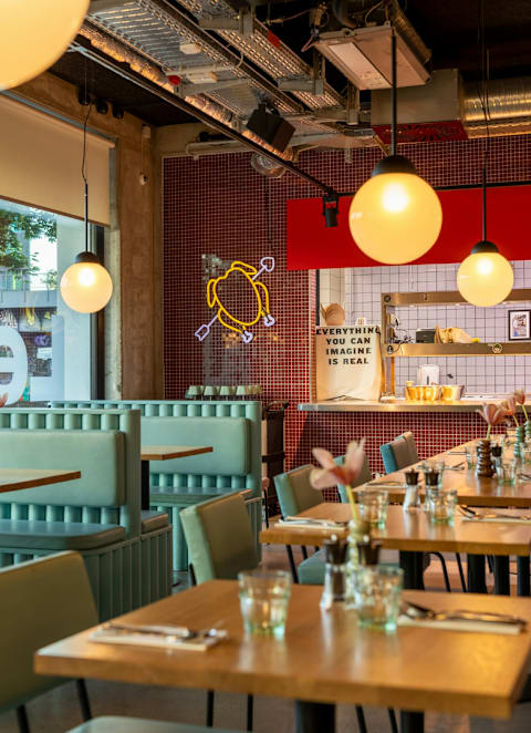 A restaurant with tables and chairs and a neon sign that says everything you can imagine is real.
