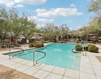 A large outdoor swimming pool surrounded by trees and lounge chairs.