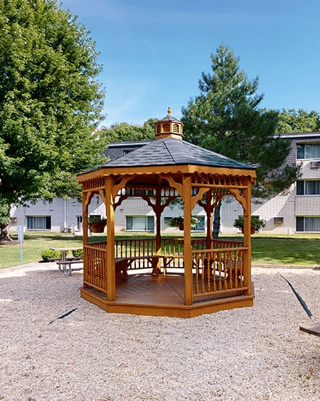 A gazebo is in the middle of a gravel area with a picnic table and benches.