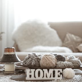 A table adorned with neutral-colored balls of yarn and a "Home" sign, adding warmth to the living room.