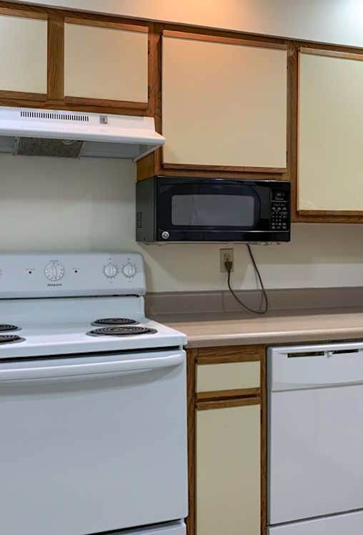 a kitchen with a white stove and dishwasher, a mounted microwave, and white and wooden cabinets