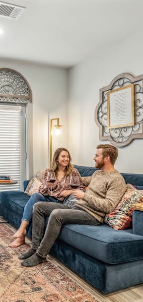 A man and woman are sitting on a blue couch in a living room with a rug on the floor.
