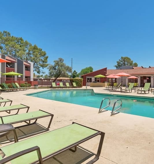 Angular shaped pool with green chaise lounge chairs facing the resident clubhouse at Spring Meadow Apartments in Glendale, Arizona