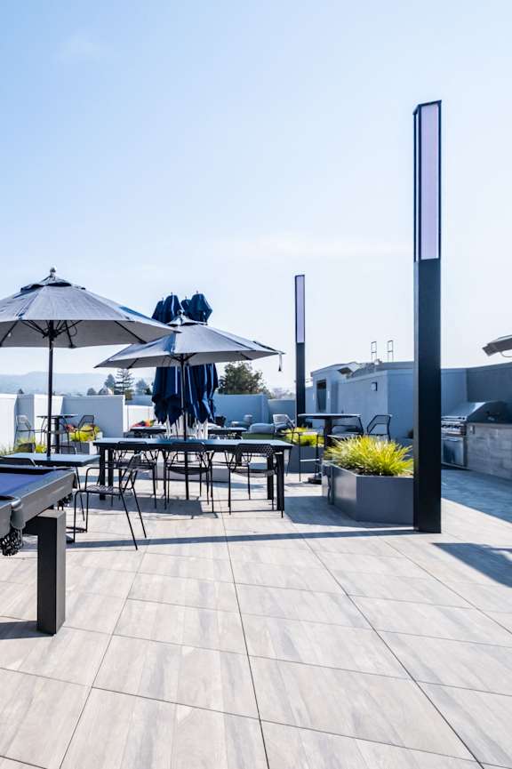 A pool table is on a patio with a table and chairs and umbrellas in the background.