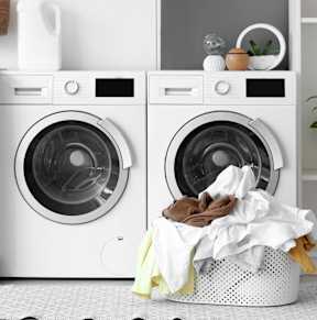 A woman is doing laundry by putting clothes into a washing machine.