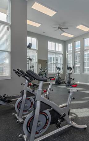 A gym with a row of stationary bikes and a fan.
